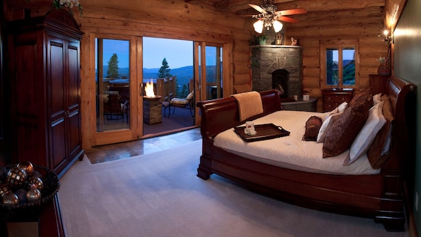 Une chambre dans un chalet en rondins avec une cheminée, un lit doté d’une tablette et une vue sur l’extérieur.