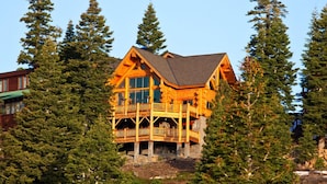 Une cabane en rondins dotée d’un balcon, entourée de grands pins.