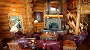 L’intérieur d’une cabane en rondins, avec une cheminée, des meubles en cuir et un escalier en bois.