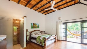 Une chambre à coucher avec un cadre de lit en bois, une grande fenêtre donnant sur un beau paysage et un ventilateur de plafond.