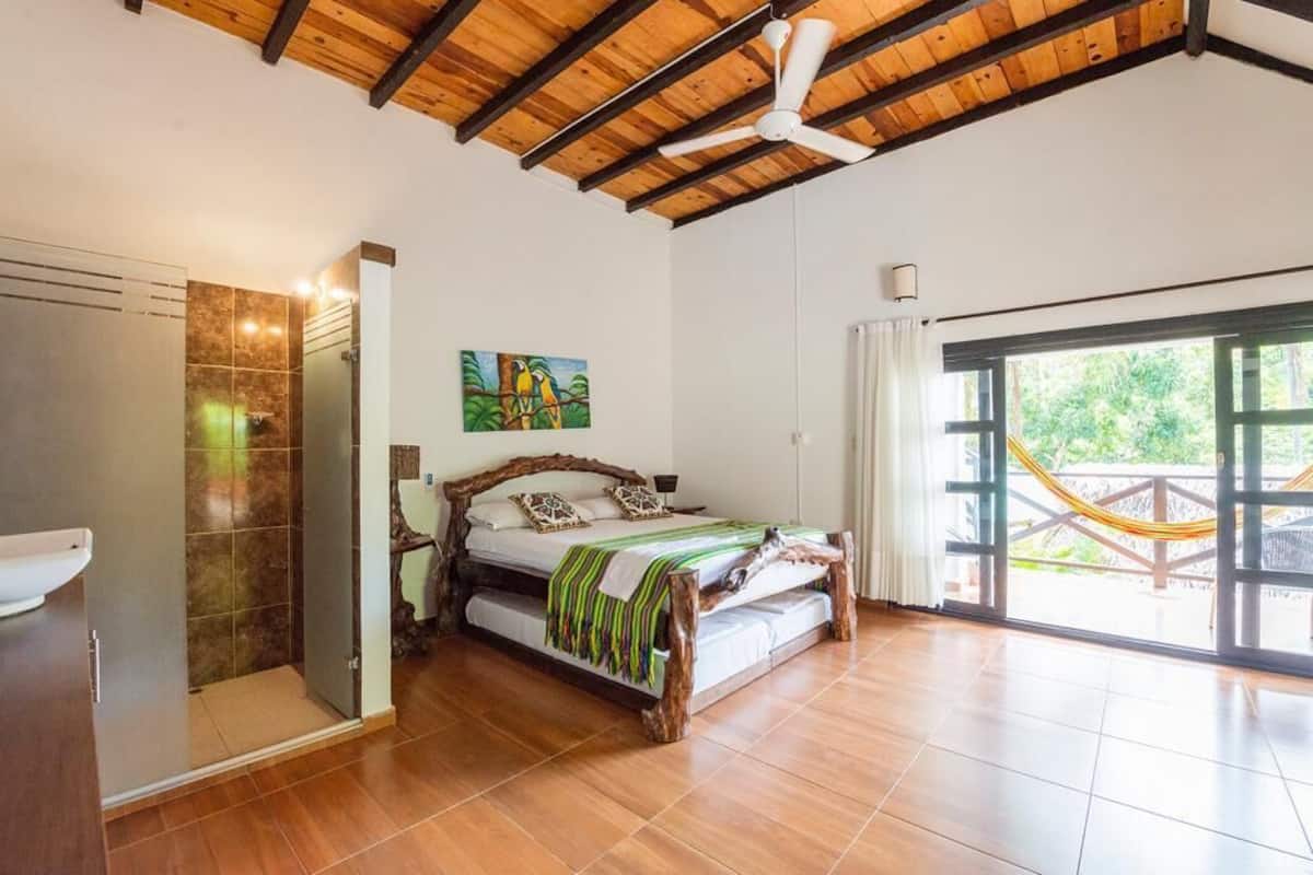 A bedroom with a wooden bed frame, a large window with a view, and a ceiling fan.