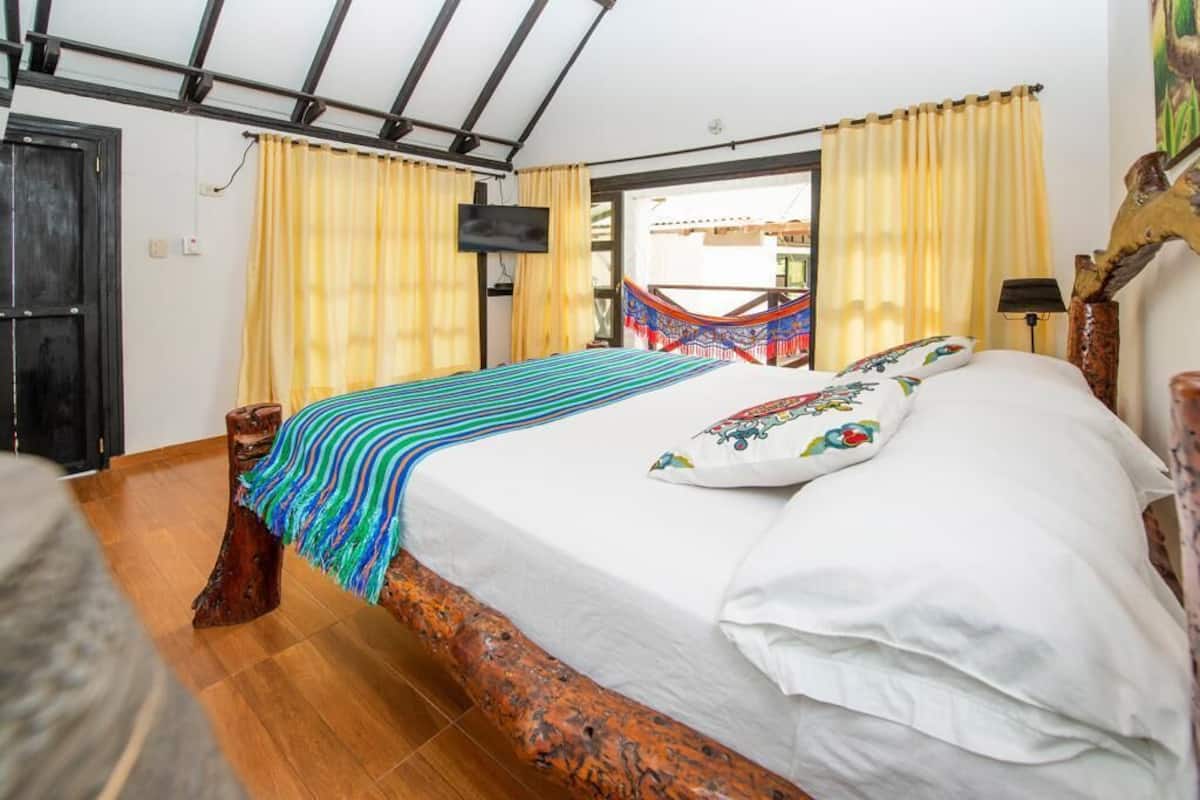 A bedroom with a wooden bed frame, a hammock, and a TV on the wall.