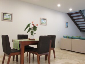 Un comedor con una mesa de madera, cuatro sillas y una planta en maceta. Hay dos cuadros colgados en la pared.