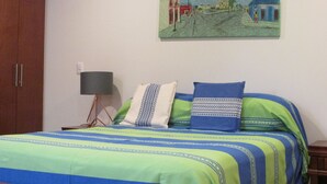 Un dormitorio con cama, mesita de noche, lámpara y un cuadro en la pared.