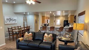 A living room with a black leather sofa, wooden dining table, and a coffee table with a board game. - THREE KING BEDS! Parking, CLEAN, Views, FIREPIT, Pool, Hot Tub, ACCESSIBLE! (Moab)