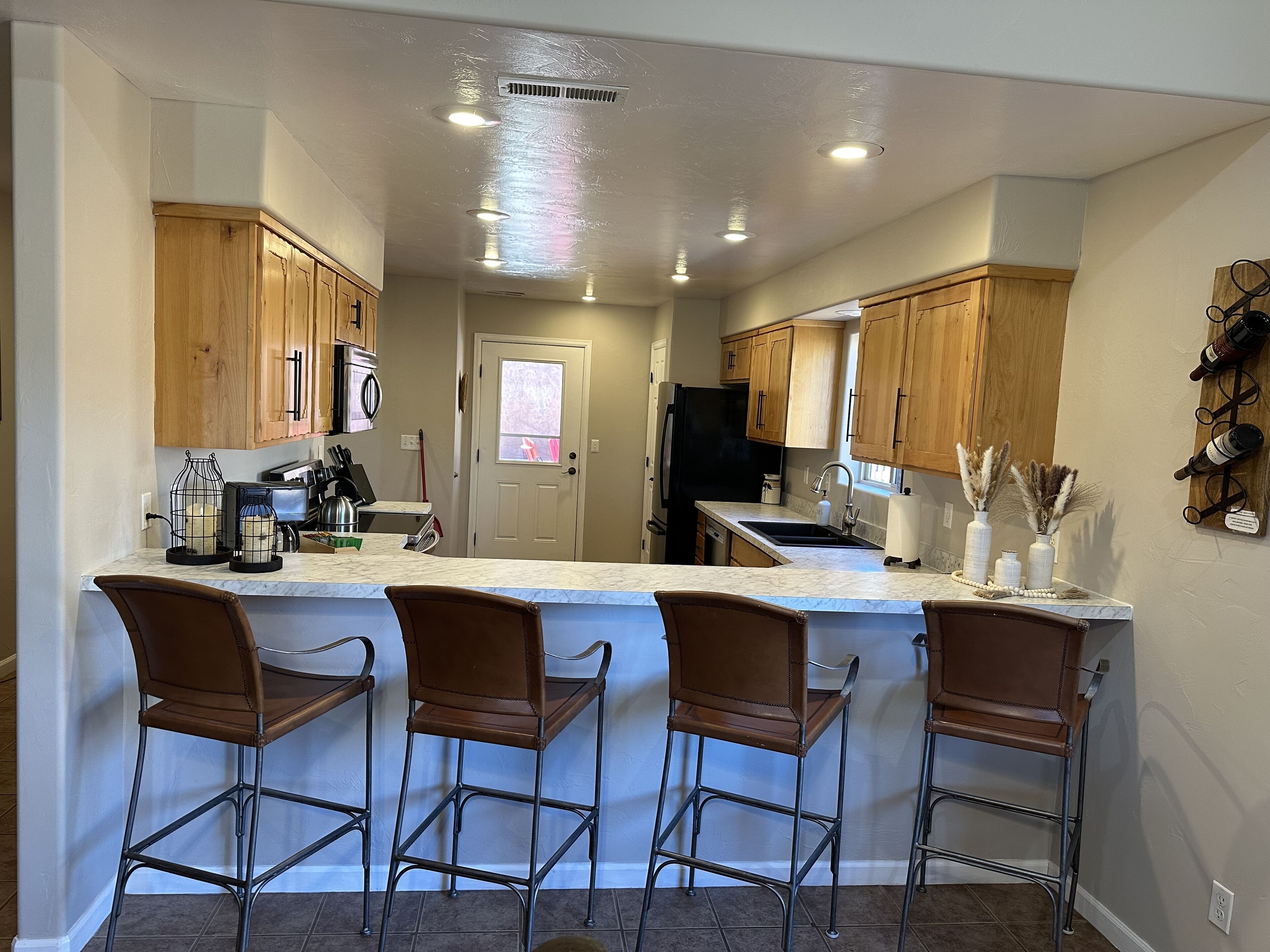 A kitchen with wooden cabinets, a marble countertop, and three bar stools.