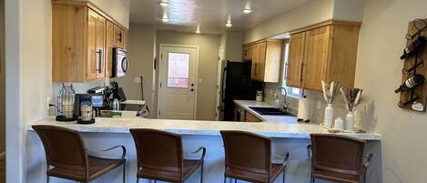 A kitchen with wooden cabinets, a marble countertop, and three bar stools.