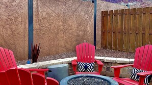 A patio with red Adirondack chairs, a fire pit, and a view of a mountainous landscape. - THREE KING BEDS! Parking, CLEAN, Views, FIREPIT, Pool, Hot Tub, ACCESSIBLE! (Moab)