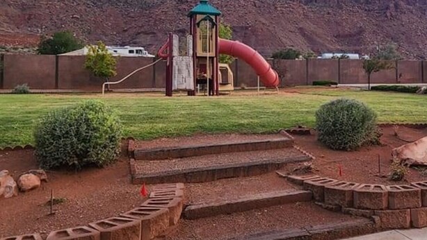 A playground with a slide and climbing structures, surrounded by a landscaped garden with steps leading up to it. - THREE KING BEDS! Parking, CLEAN, Views, FIREPIT, Pool, Hot Tub, ACCESSIBLE! (Moab)