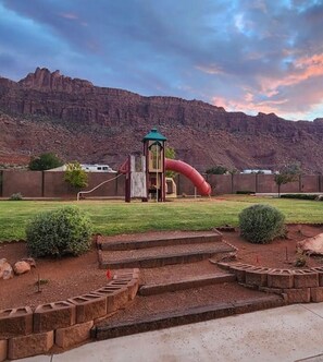 A playground with a slide and climbing structures, surrounded by a landscaped garden with steps leading up to it. - THREE KING BEDS! Parking, CLEAN, Views, FIREPIT, Pool, Hot Tub, ACCESSIBLE! (Moab)
