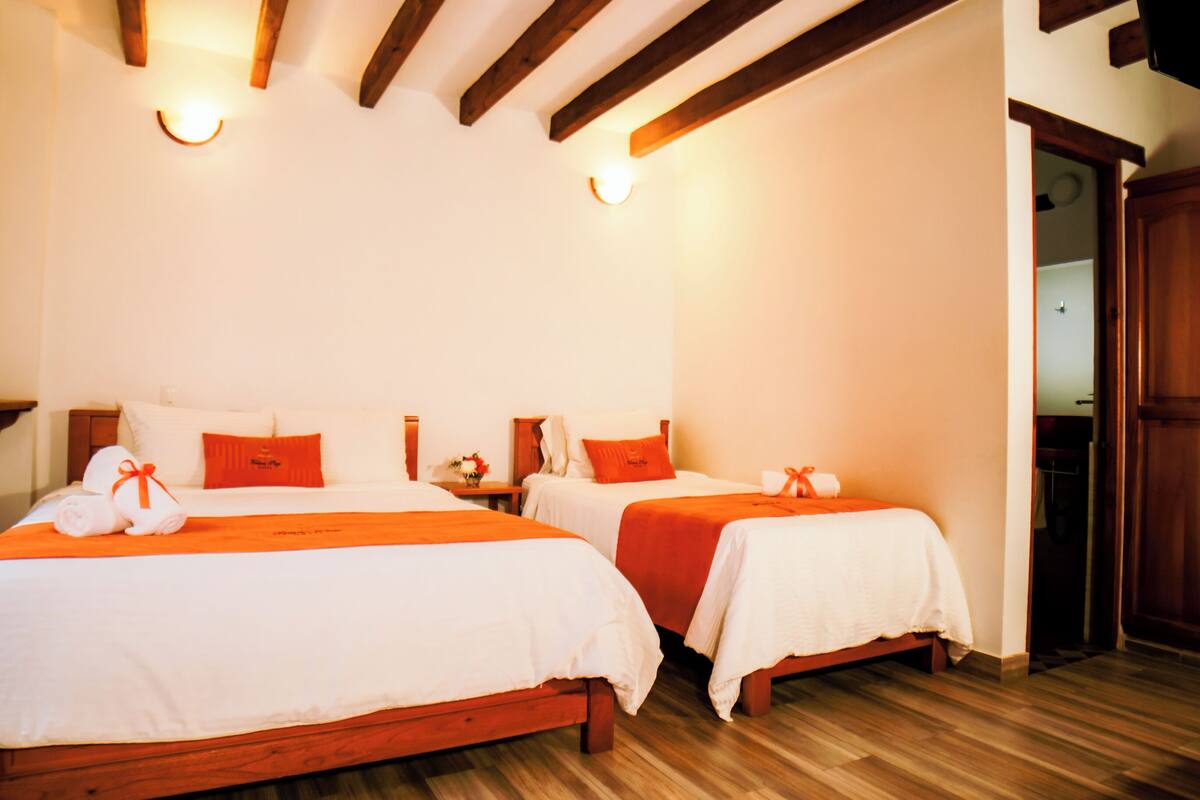 Une chambre d’hôtel avec deux lits, des têtes de lit en bois, du linge de lit blanc et des touches de couleur orange.