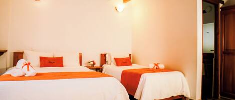 Habitación de hotel con dos camas, cabeceros de madera, ropa de cama blanca y detalles en naranja.