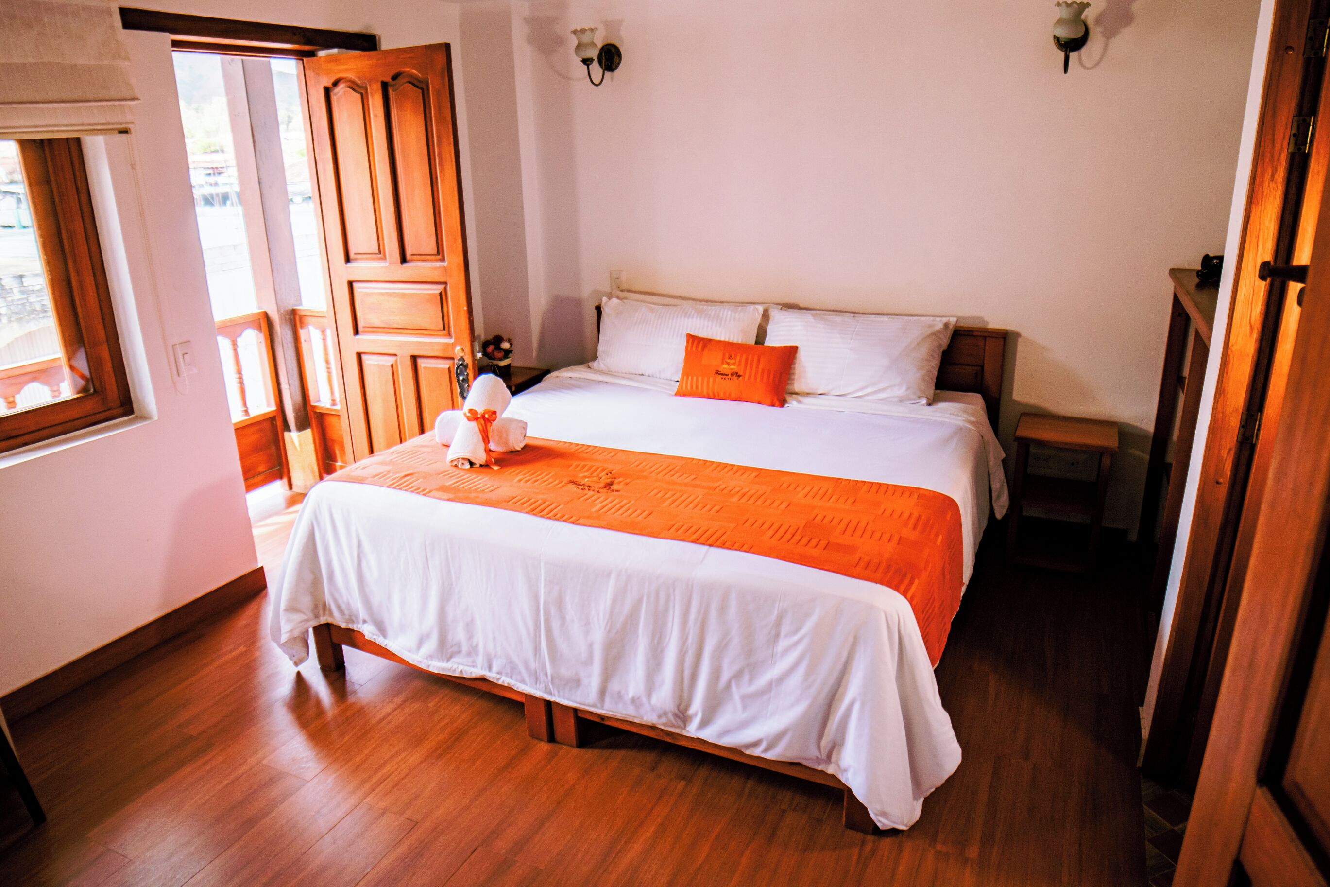 Un dormitorio con cama de madera, ropa de cama blanca, un plaid naranja y una mesita de noche.