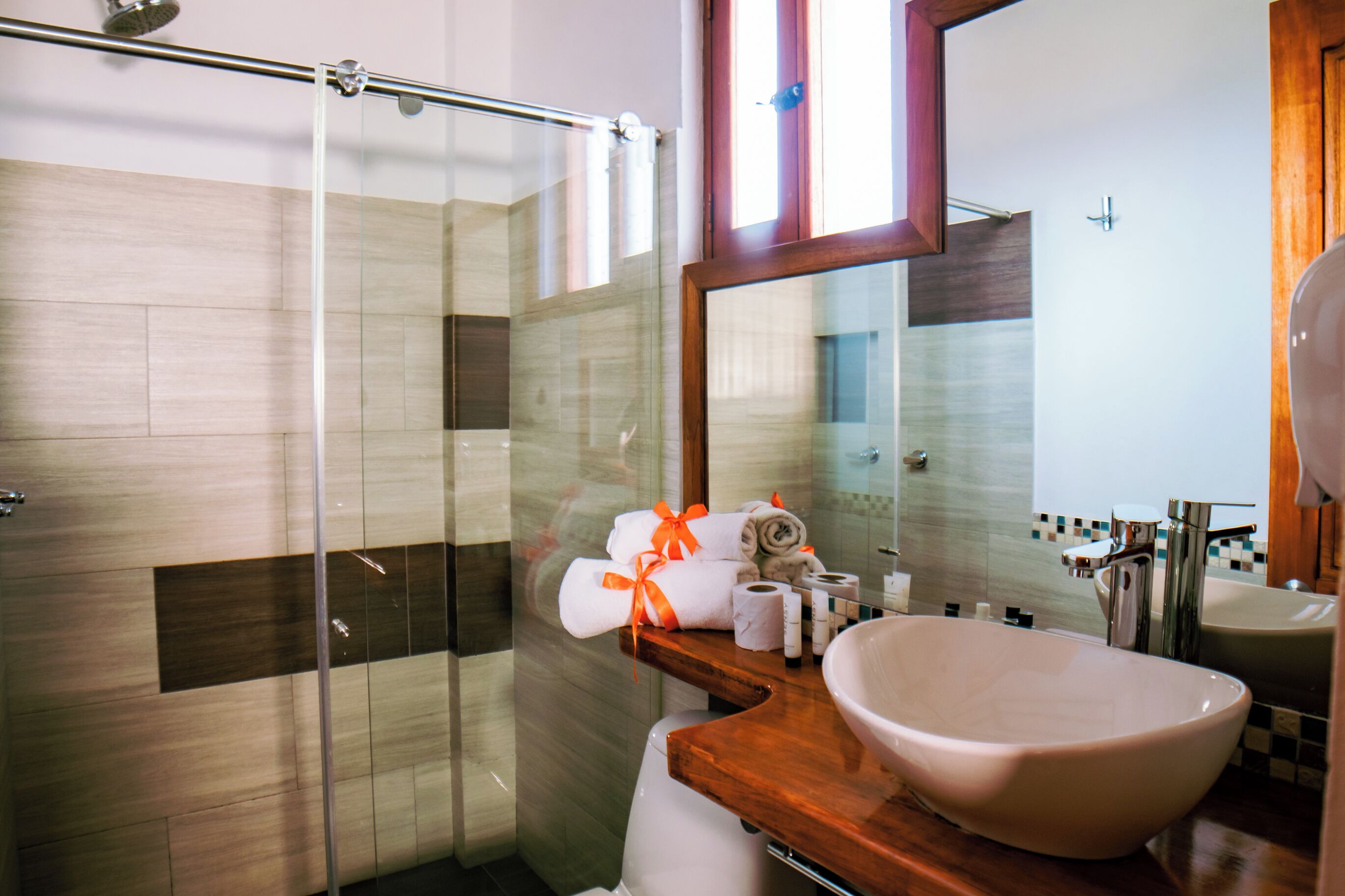 Une salle de bain moderne avec une douche à l’italienne en verre, un meuble-lavabo en bois avec un grand lavabo blanc et un miroir au-dessus du lavabo.