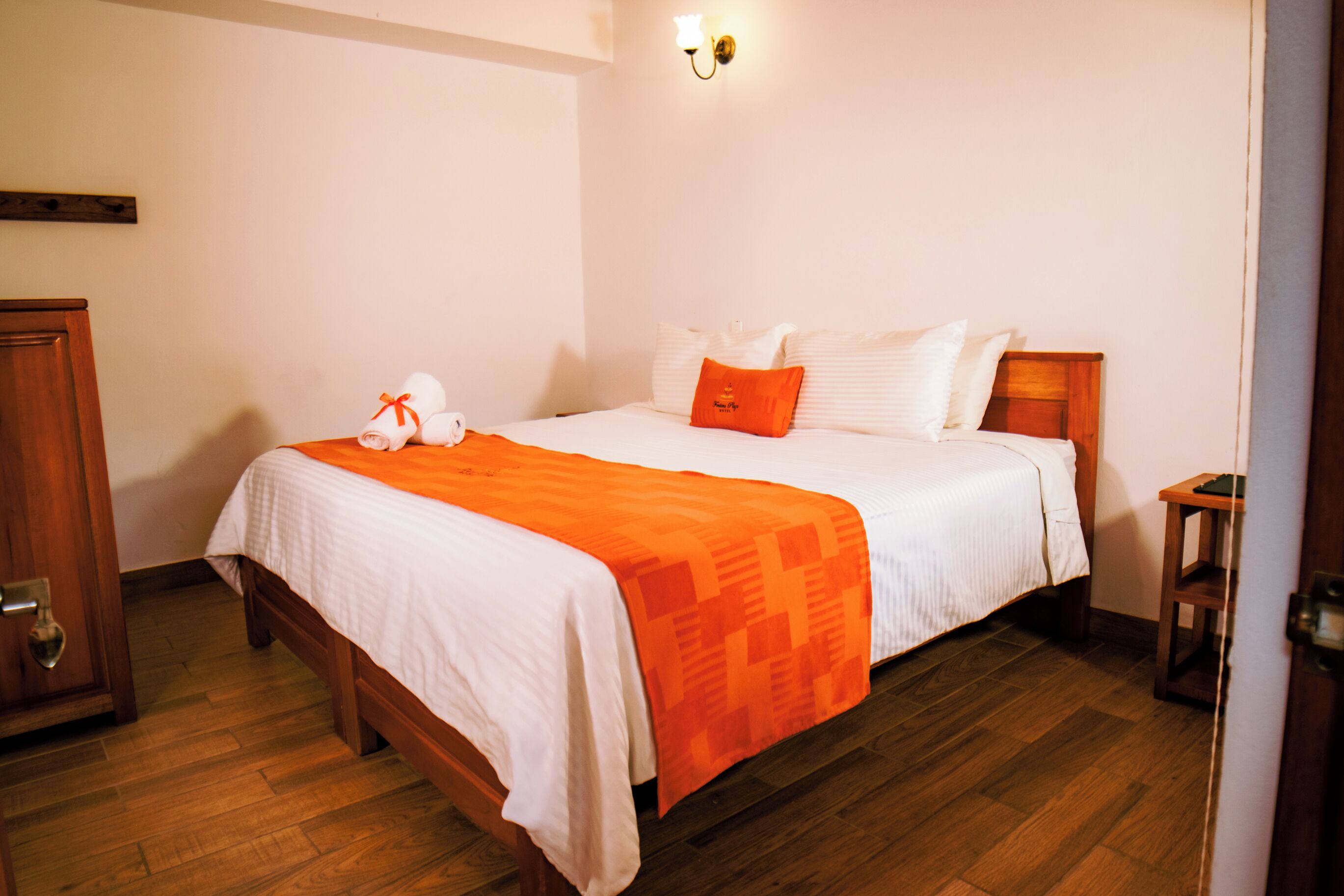 A neatly made bed with a white and orange bedspread, a wooden headboard, and a small bedside table with a lamp.