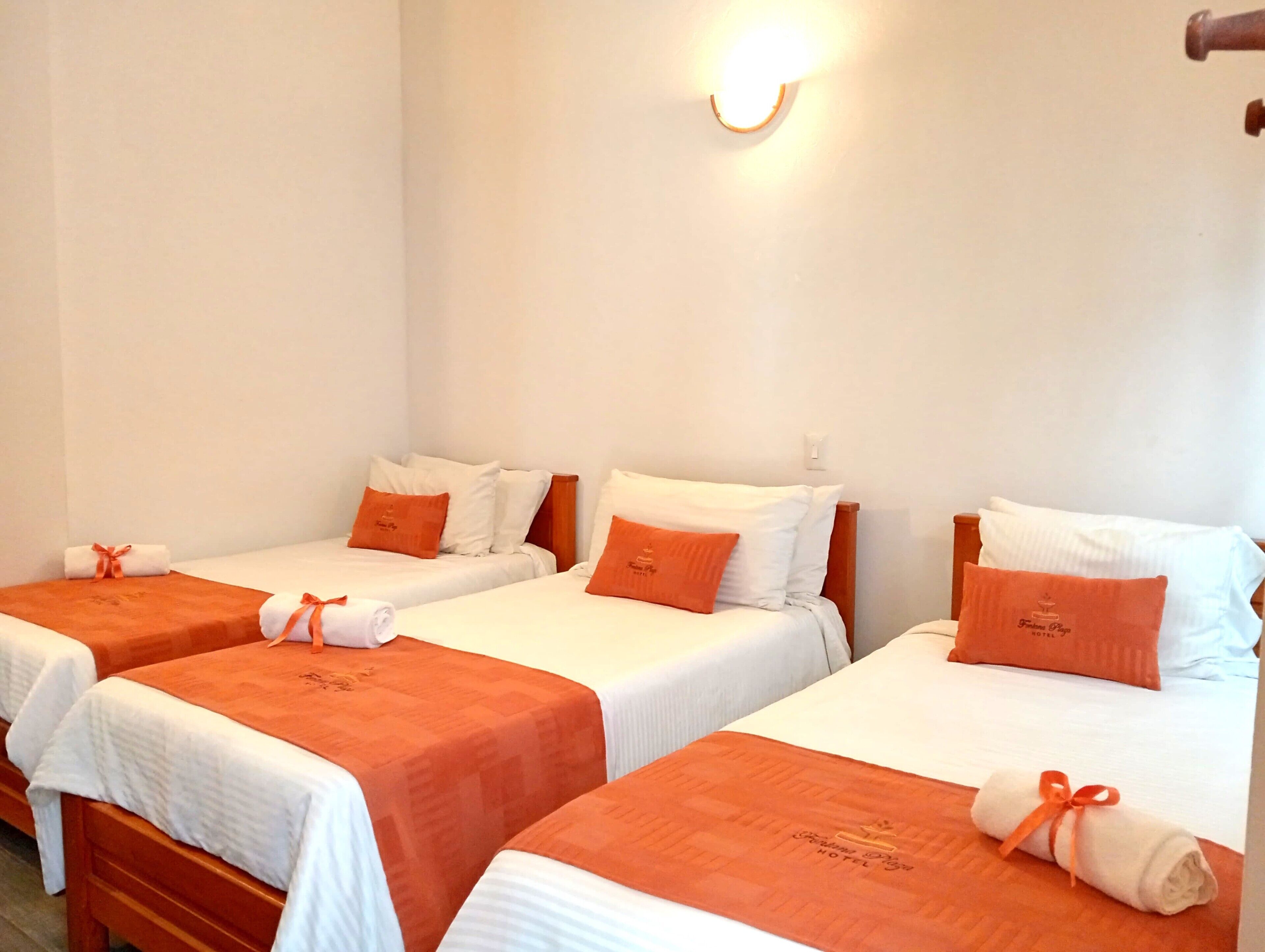A hotel room with three single beds, each with an orange bedspread and matching pillows.