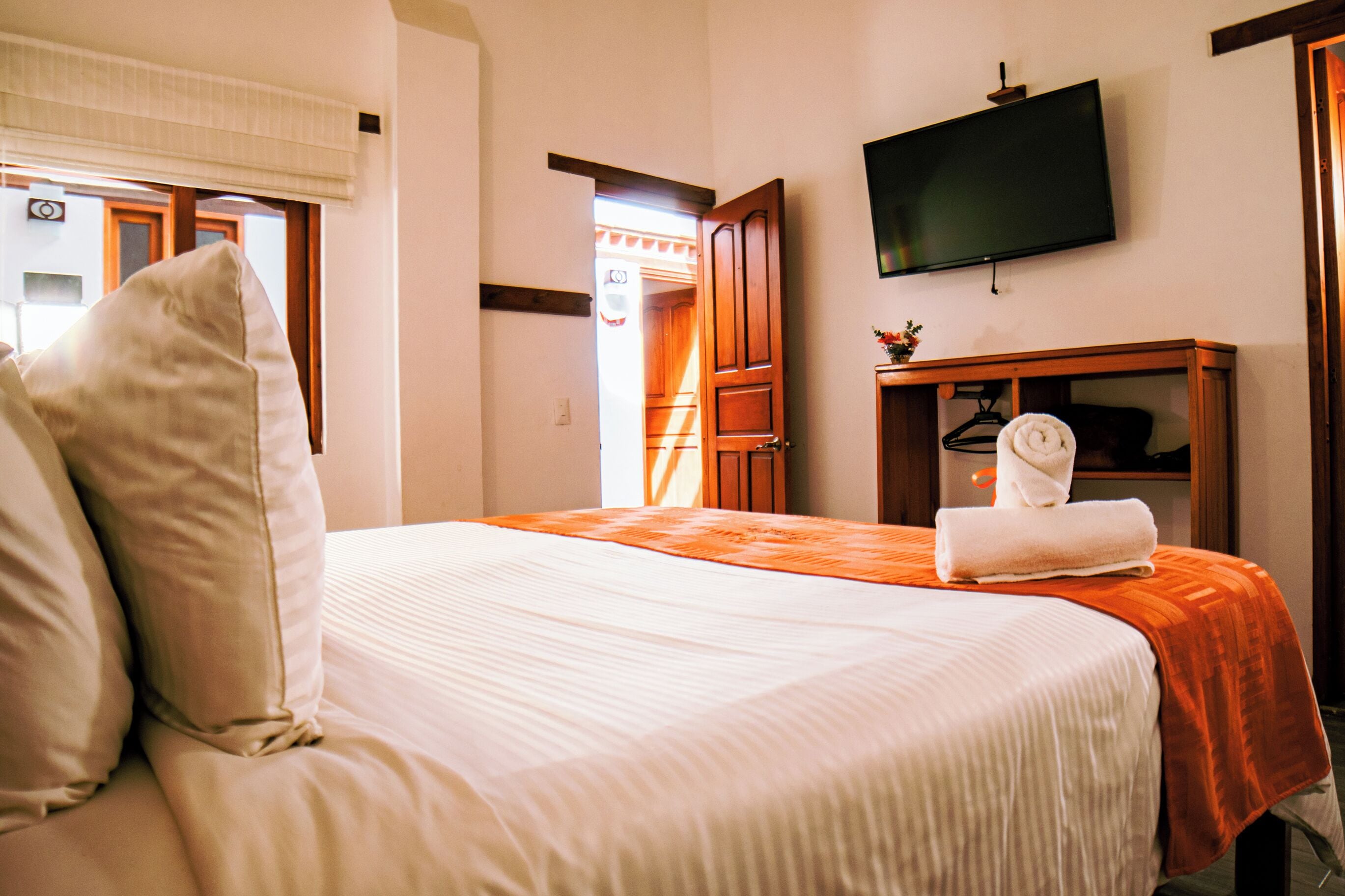 Una habitación de hotel con una cama, un televisor montado en la pared y un armario de madera con una toalla.