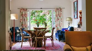 A cozy living room with a dining table, chairs, and a view of a garden through large windows. - Very spacious rural retreat, walk to Crieff — Couples, Families, Pets Welcome. (Crieff)