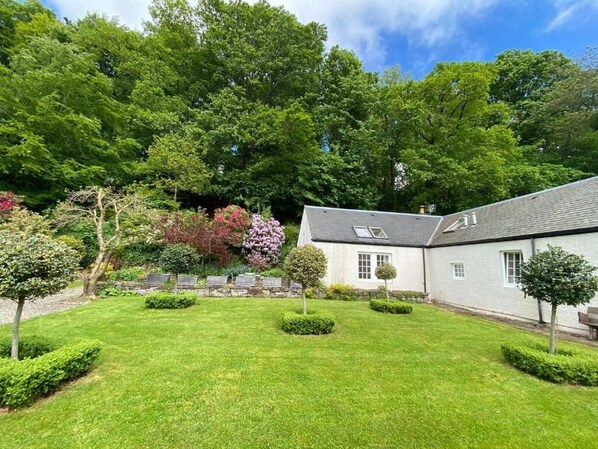 A white building with a sloped roof and a small garden area with trimmed hedges and trees. - Very spacious rural retreat, walk to Crieff — Couples, Families, Pets Welcome. (Crieff)