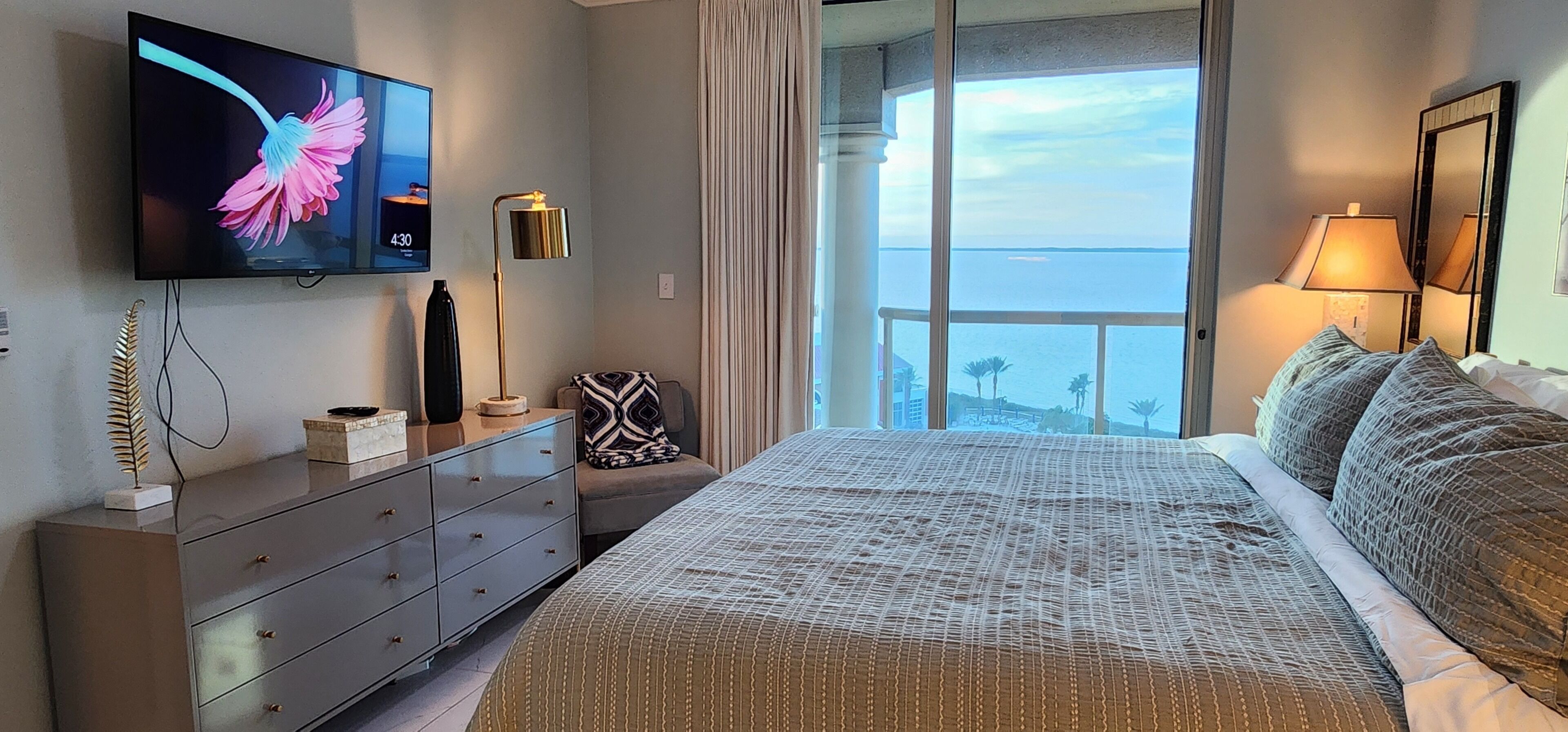 Un dormitorio con una cama grande, un televisor en la pared, un aparador y vistas al océano.
