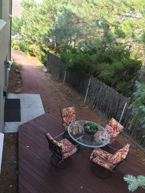 Eine Terrasse mit einem Tisch aus Glasplatte und vier stuhlähnlichen Sitzgelegenheiten mit Blumenmuster, umgeben von einem Holzzaun und Bäumen.