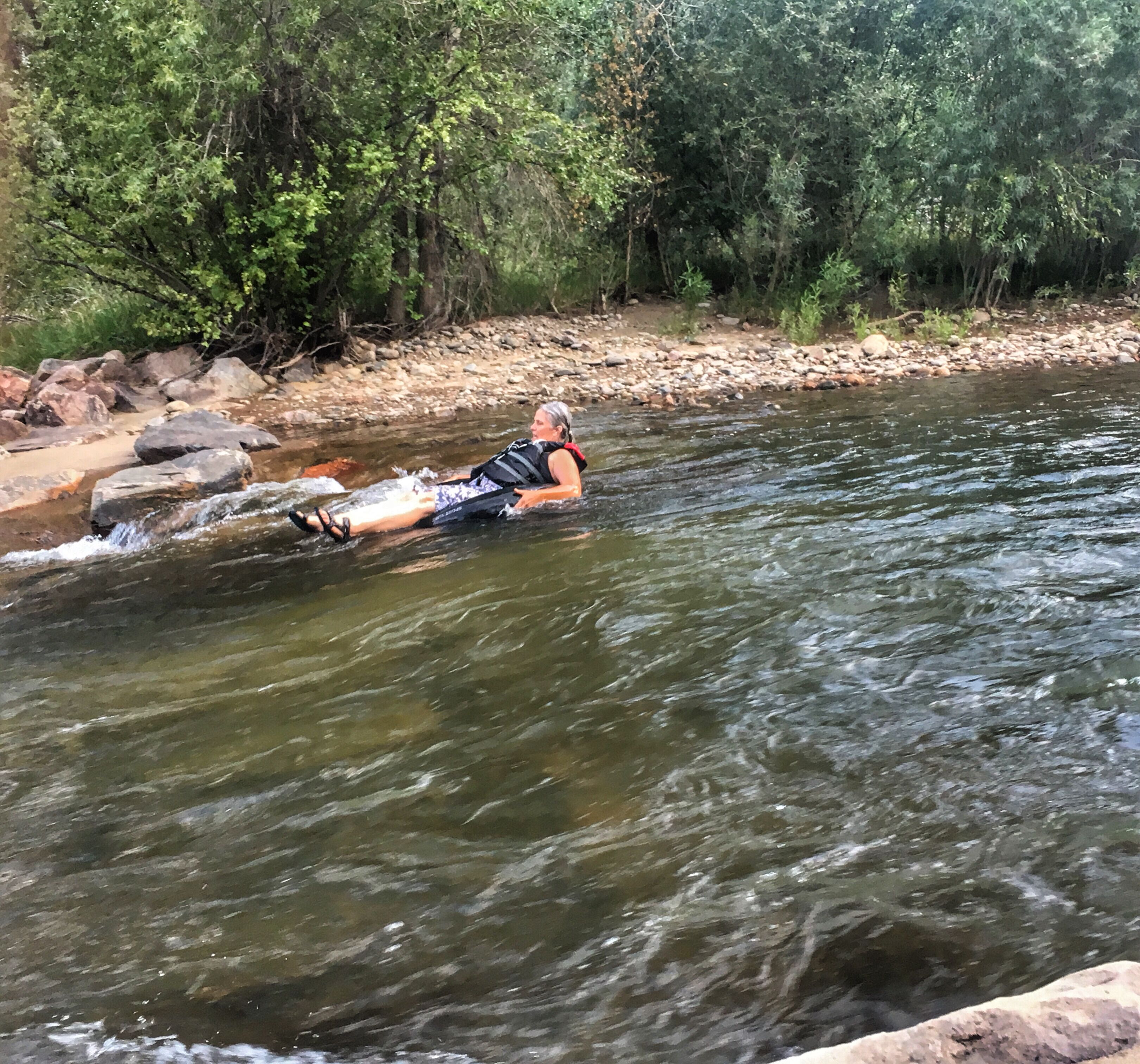 Una persona galleggia su un tronco in un fiume, circondata da rocce e alberi.