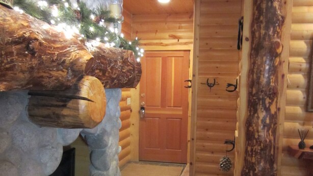 A log cabin interior with a stone fireplace, wooden walls, and a wooden door.