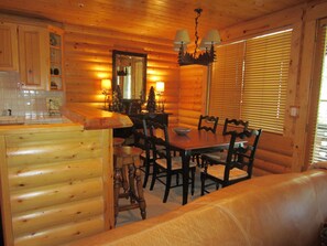 L’intérieur d’une cabane en rondins, avec une table à manger en bois, des chaises, un canapé et un coin cuisine doté de placards et d’un plan de travail.