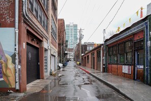 Une rue étroite en milieu urbain, bordée de bâtiments des deux côtés, certains affichant des enseignes visibles et d’autres avec des fenêtres condamnées.