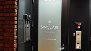 Un ascensor moderno con un panel de vidrio que muestra el nombre 'SINCLEAR' y una dirección web.