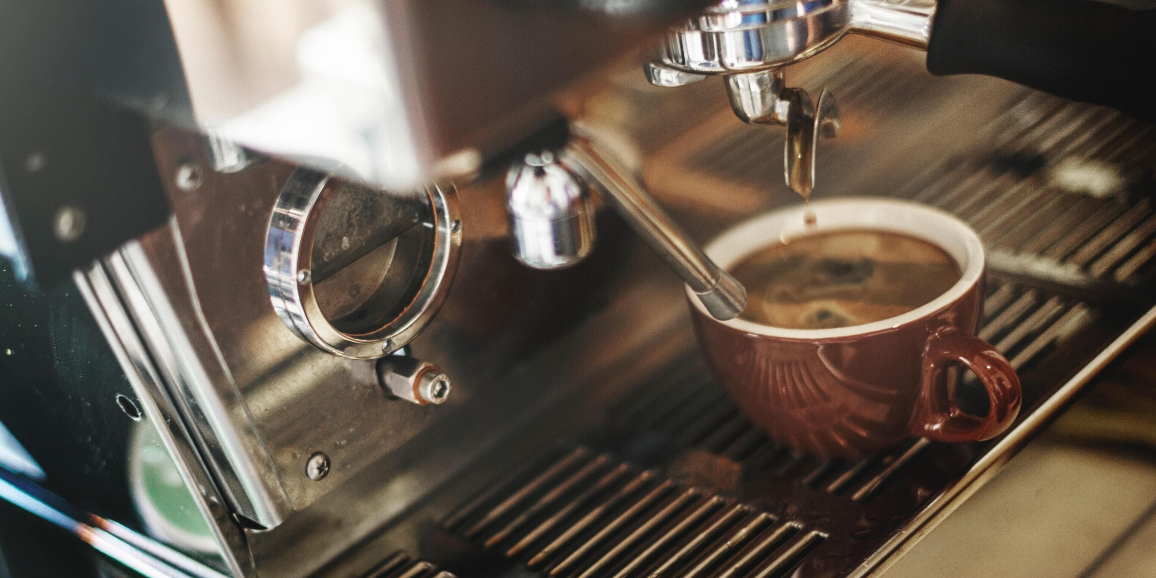 Gros plan d’une machine à expresso avec une tasse rouge posée sur le bac d’égouttement.
