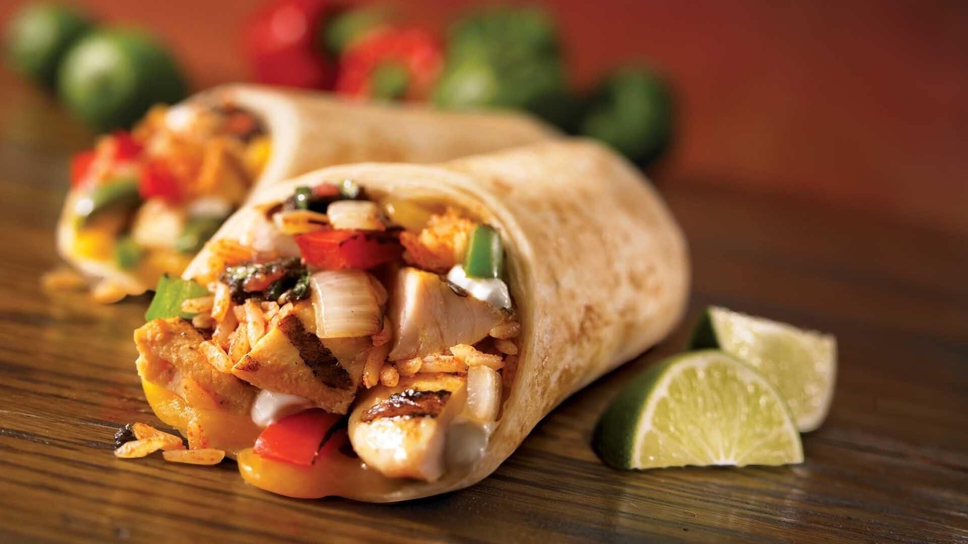 Un burrito con relleno visible de pollo, arroz y verduras, acompañado de una cuña de limón sobre una superficie de madera.