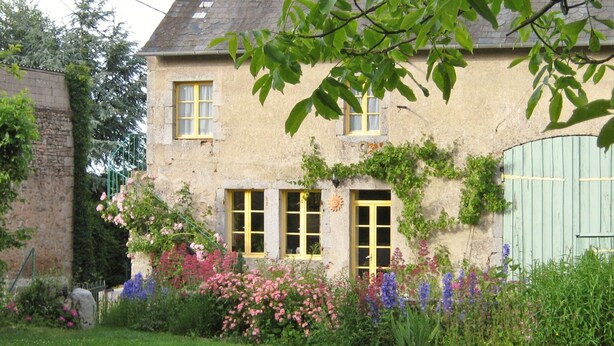 A stone house with a garden, featuring a green door, yellow windows, and a blue gate.