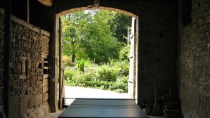 A room with a table in the center, stone walls, and a view of greenery outside.