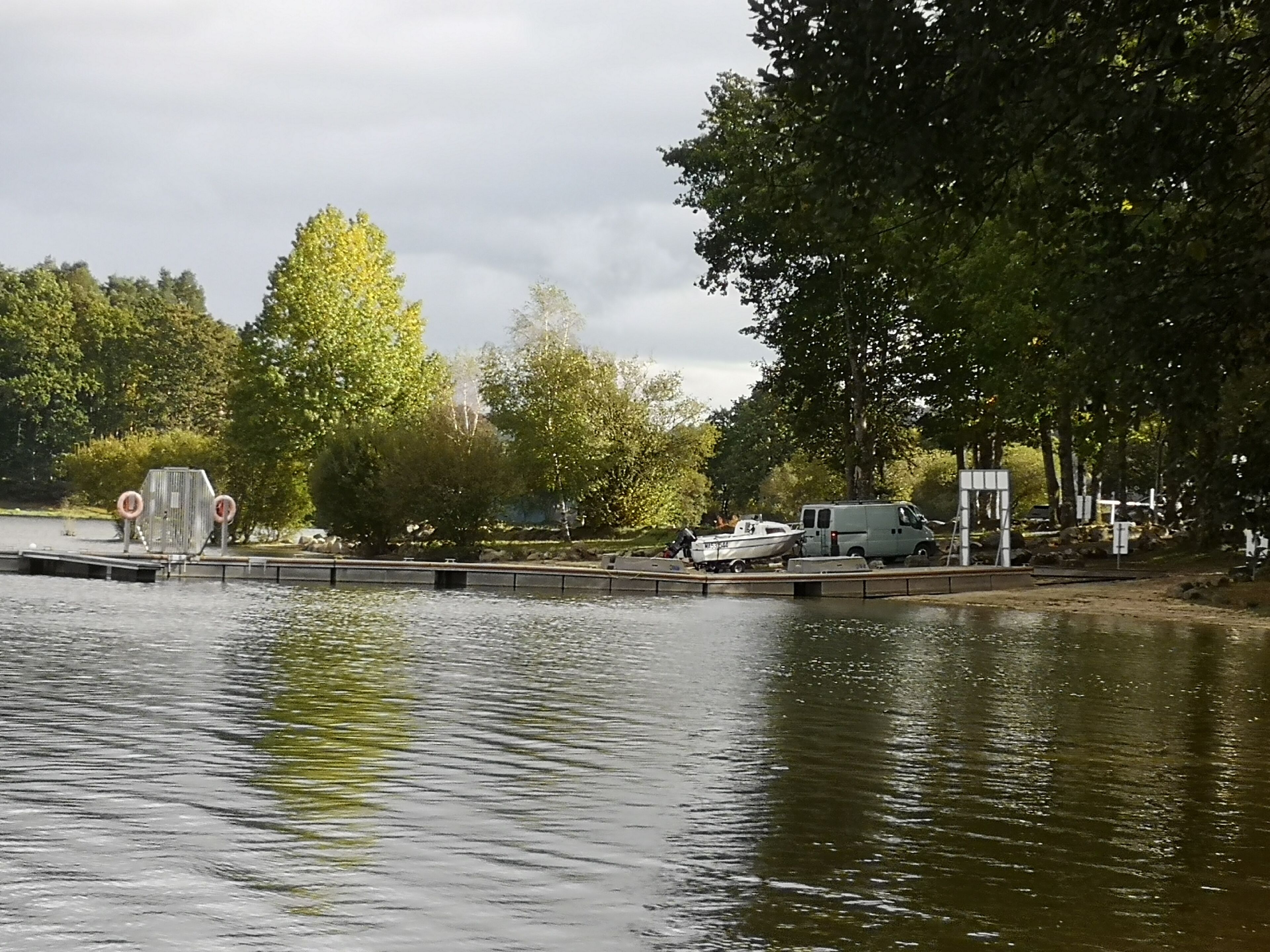 Ein ruhiger See mit einer Anlegestelle, einem Boot und einem in der Nähe geparkten Wagen.