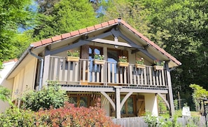 A two-story wooden house with a balcony, large windows, and a red roof.