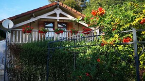 Una casa con techo inclinado, barandillas blancas y flores rojas en macetas.