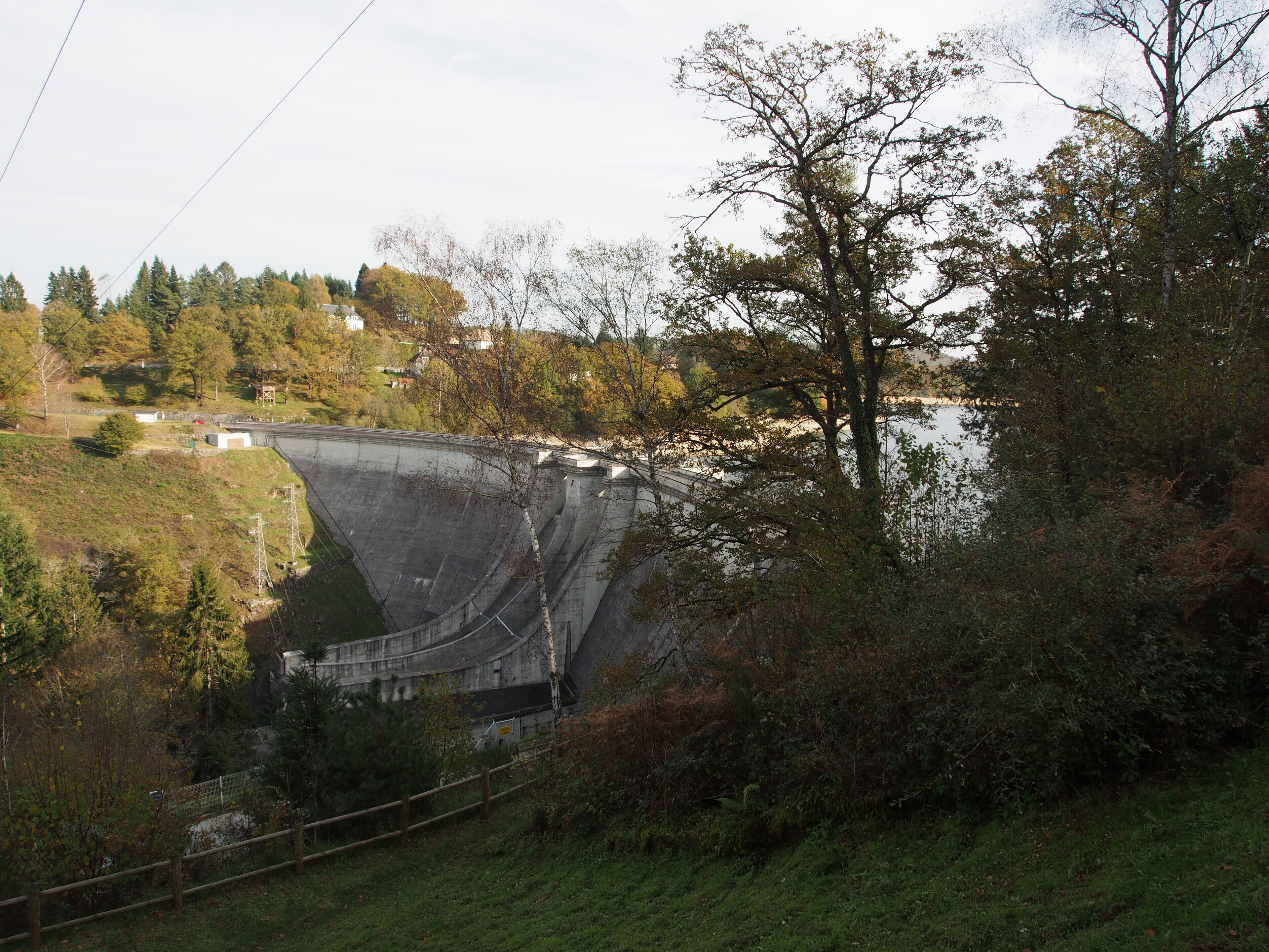 A large dam with a spillway, surrounded by trees and a small building.