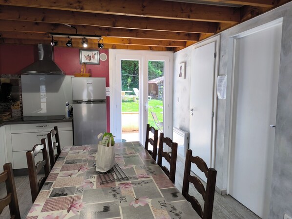 A kitchen with a refrigerator, stove, and a dining table with chairs.