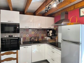 Une cuisine avec des armoires blanches, un four à micro-ondes de marque Bosch, une hotte de cuisinière en acier inoxydable et un réfrigérateur.
