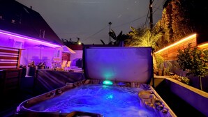 Un jacuzzi con panel de control, rodeado de mobiliario y plantas de exterior.