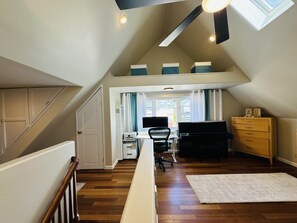 Un dormitorio estilo loft con techo inclinado, suelo de madera, un escritorio con silla, cómoda y ventana con cortinas.