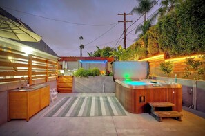 A modern outdoor hot tub area with a wooden deck, a built-in seating area, and a wall-mounted TV.