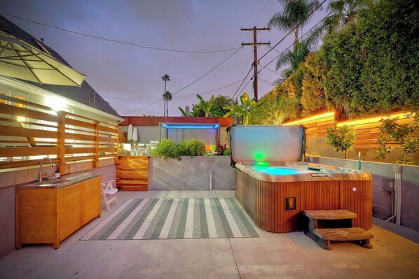 Un área moderna de hidromasaje al aire libre con un deck de madera, una zona de estar integrada y un televisor montado en la pared.