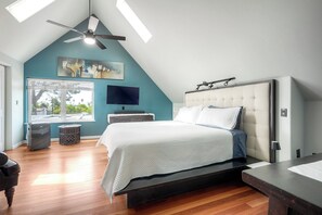 Un dormitorio con cama, televisión, ventilador de techo y ventana con vistas.