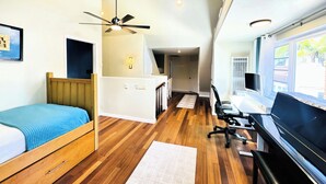 Una habitación de hotel pequeña con cama, escritorio, computadora, piso de madera y ventilador de techo.