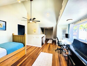 Una habitación de hotel pequeña con cama, escritorio, computadora, piso de madera y ventilador de techo.