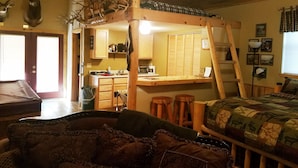 Ein rustikales Blockhaus-Interieur mit Schlafkoje, Holzmöbeln, einer Küchenzeile und Dachhirschen an der Wand.