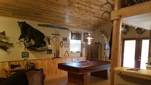 Ein Holzinterieur mit Billardtisch, einer Couch und verschiedenen aufgehängten Tierköpfen an den Wänden.