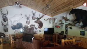 Ein Zimmer mit Holzboden, einem Fernseher, einer Couch und verschiedenen aufgehängten Tierköpfen an den Wänden.